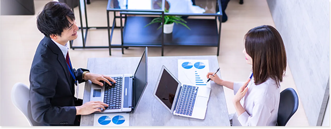 デスクで向かい合っている男女。デスクにパソコンを広げている。